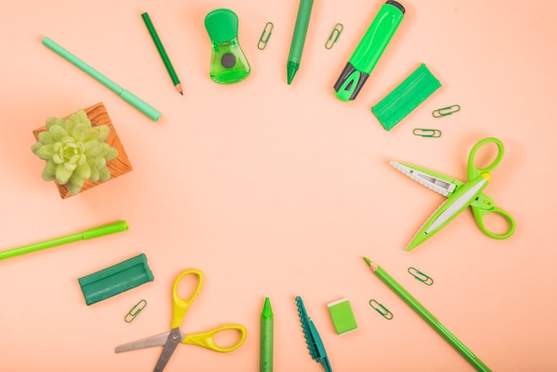 Foto gratuita forniture di cancelleria e piante in vaso che formano una cornice circolare su una superficie colorata