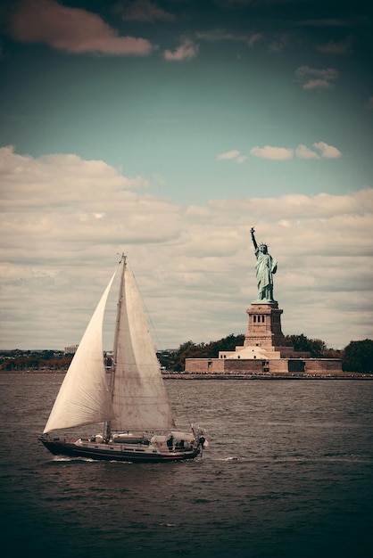 Statue of Liberty at New York City harbor with sailing boat.