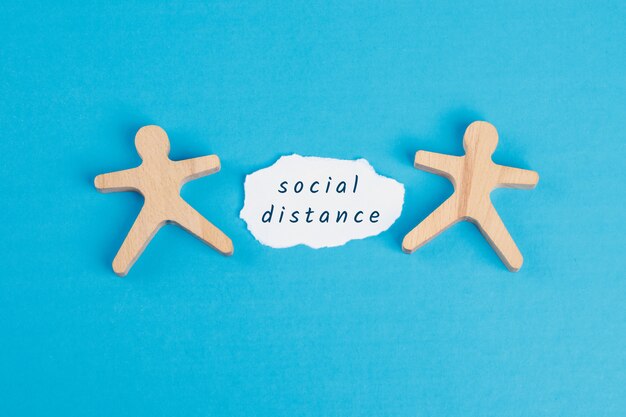 Stay at home concept with social distance text on torn paper, wooden figures on blue table flat lay.