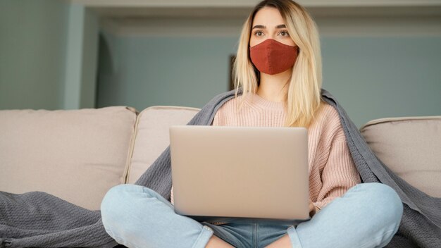 Stay indoors woman wearing medical mask and holding laptop