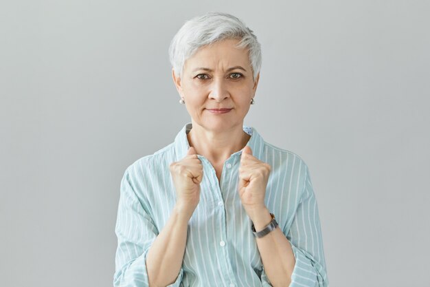 Stay strong. self determined grandmother in stylish shirt keeping fists clenched encouraging her grandchild. Senior female winner clenching fists, expressing joy and excitement