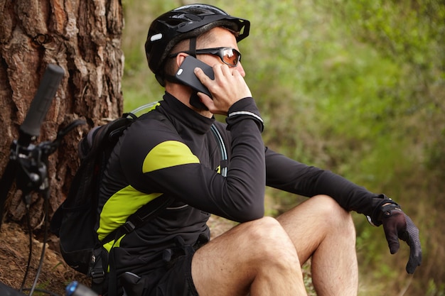 Staying connected. Cropped shot of handsome young European biker wearing helmet and eyeglasses talking on mobile phone