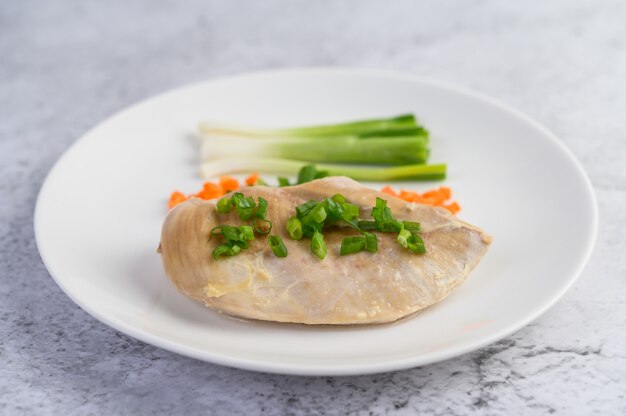 Паровая куриная грудка на белой тарелке с зеленым луком и нарезанной морковью
