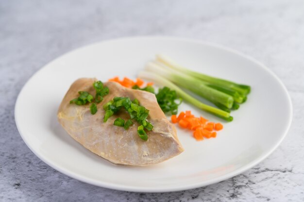 Steamed chicken breast on a white plate with spring onions and chopped carrots