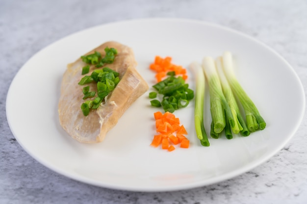 Steamed chicken breast on a white plate with spring onions and chopped carrots