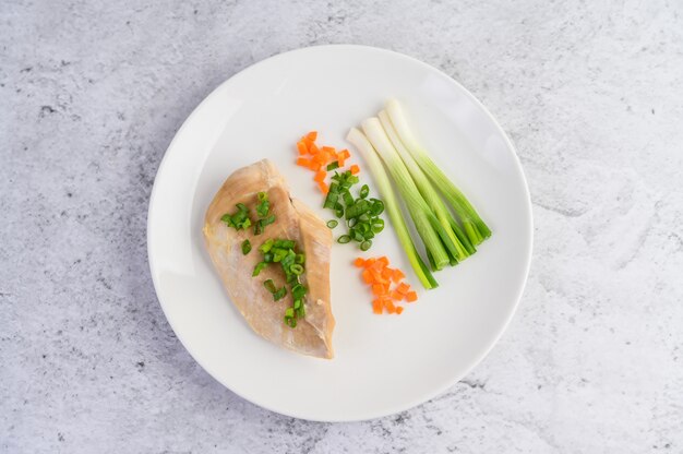 Steamed chicken breast on a white plate with spring onions and chopped carrots