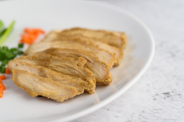 Steamed chicken breast on a white plate with spring onions and chopped carrots