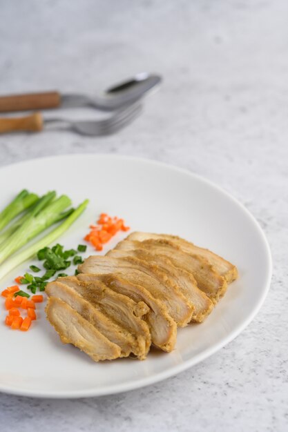 Steamed chicken breast on a white plate with spring onions and chopped carrots