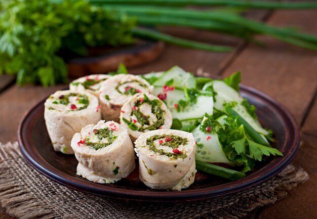 Steamed chicken rolls with greens and fresh vegetable salad on a brown plate