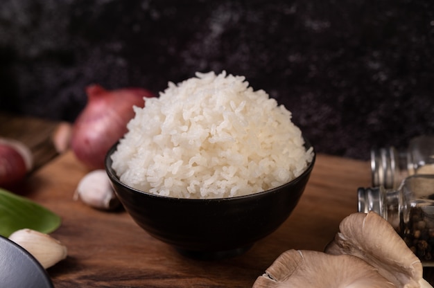 Пропаренный рис в миске с чесноком и красным луком на деревянной разделочной доске