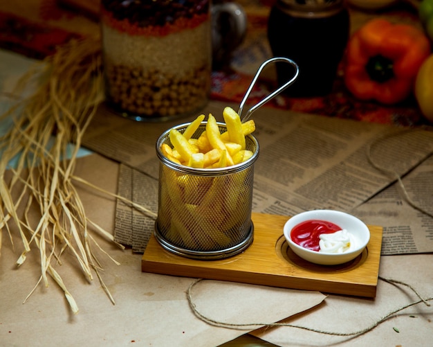 A steel basket of french fries served with ketchup and mayonnaise