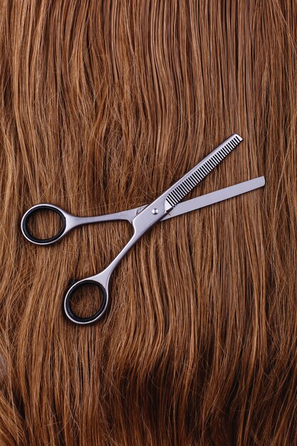 Steel scissors lie on the wave of silk brown hair