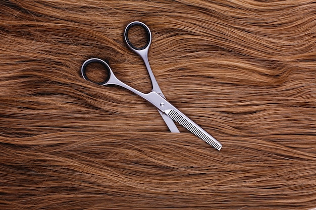 Free photo steel scissors lie on the wave of silk brown hair