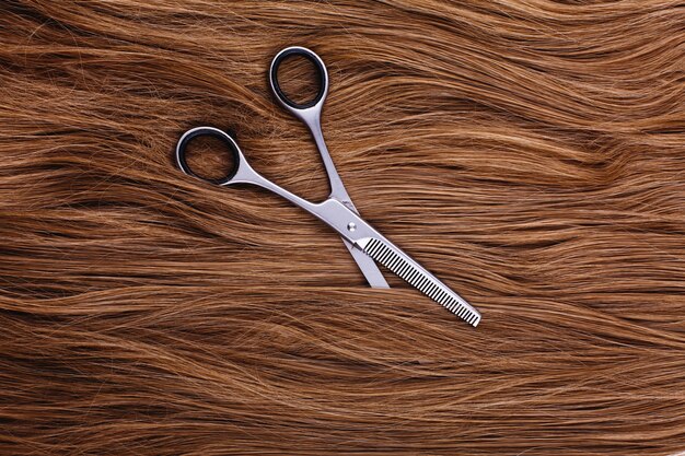 Steel scissors lie on the wave of silk brown hair