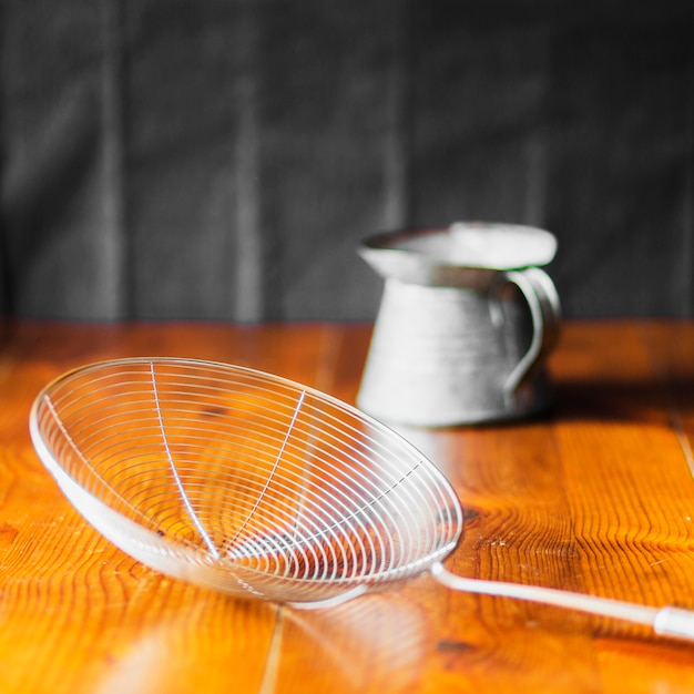 Free photo steel skimmer in front of old jug on wooden table