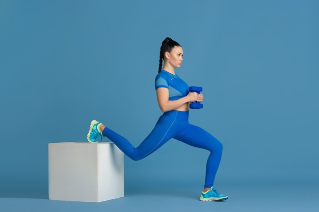 Stepping. Beautiful young female athlete practicing , monochrome blue portrait. Sportive fit brunette model with jump box, weights. Wellness, healthy lifestyle, beauty and action concept.