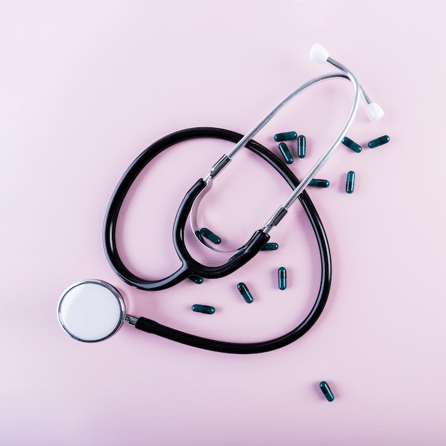 Stethoscope and capsules over pink background