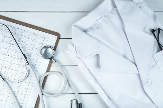 stethoscope,clipboard and doctor’s uniform on white neat wooden desk