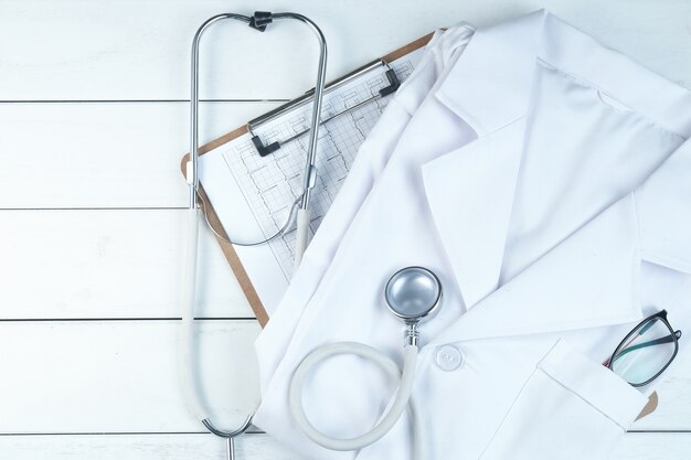 stethoscope,clipboard and doctor’s uniform on white neat wooden desk