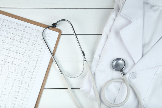 stethoscope,clipboard and doctor’s uniform on white neat wooden desk