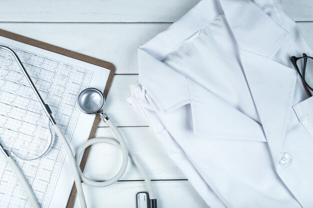 흰색 깔끔한 나무 책상에 청진 기, 클립 보드 및 의사의 유니폼