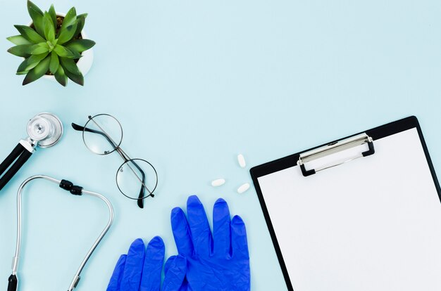 청진기; 안경; 선인장 식물; 수술 용 장갑; 약과 파란색 배경 위에 클립 보드에 종이