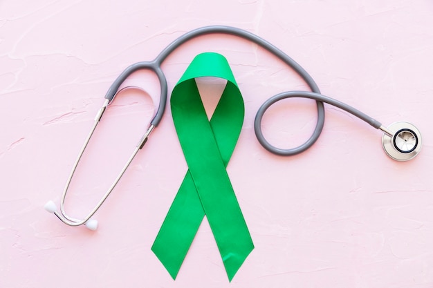 Free photo stethoscope and green awareness ribbon on pink background