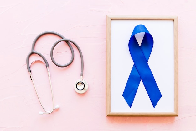 Stethoscope near the wooden frame with blue awareness ribbon