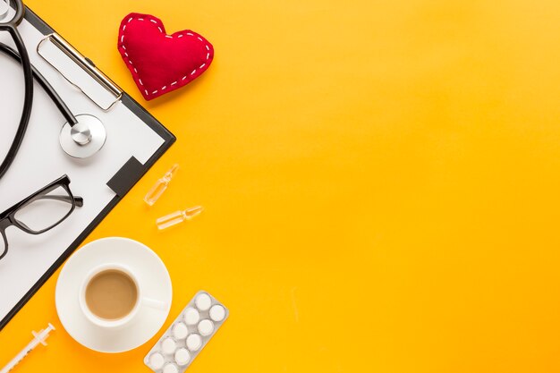 Stethoscope; stitched heart shape; coffee cup; blister packed medicine; injection over yellow backdrop