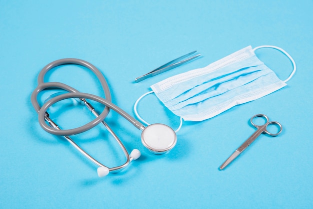 Stethoscope; surgical mask; scissor and tweezers on colored background