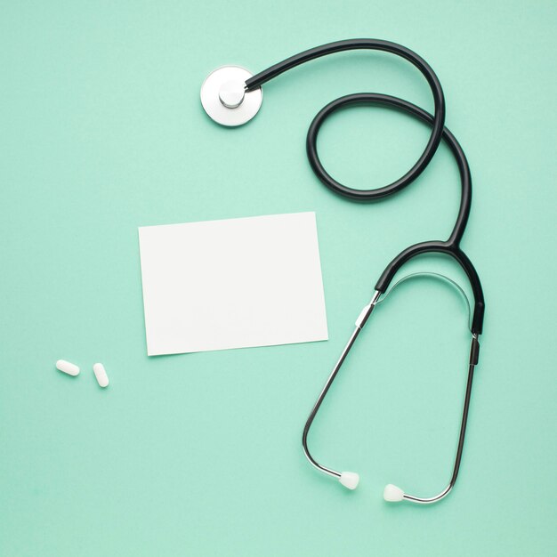 Stethoscope with blank paper and white pills over pastel green background