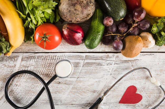 Stethoscope with heart shape near fresh vegetables on wooden background