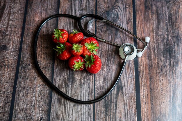 Stethoscope with strawberries and black seedless grape on top of wooden table. Medical and healthcare conceptual.