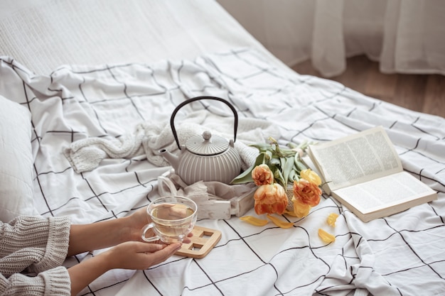 Still life with a cup of tea, a teapot, a bouquet of tulips and a book in bed