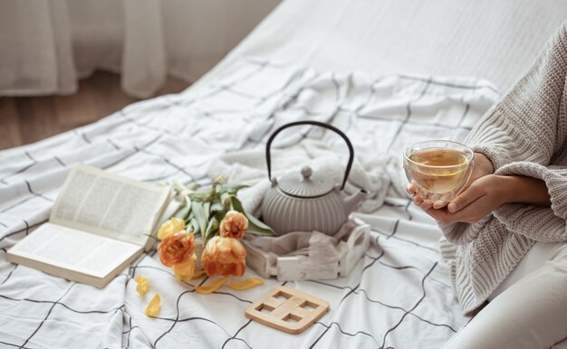 Still life with a cup of tea, a teapot, a bouquet of tulips and a book in bed