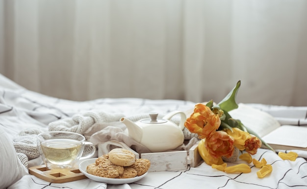 차 한잔, 주전자, 튤립 꽃다발 및 침대에서 쿠키가있는 정물