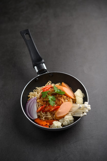 Still life with the noodles in a frying pan on the black cement floor.