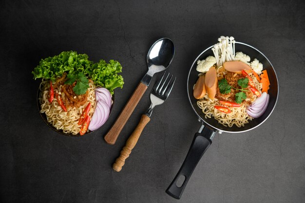 Still life with the noodles in a frying pan, fork, and spoon on the black cement floor.