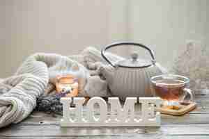 Бесплатное фото Натюрморт с чайником и чаем на деревянной поверхности с вязанным элементом, уютными деталями и декоративным словом дома