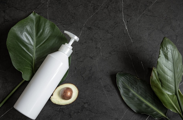 Still life with white cosmetic dispenser bottle mockup with avocado and leaves top view. Beauty and hygiene concept.