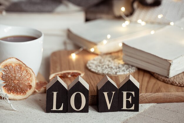 Still life with the wooden word love, a cup of drink and cozy decor details on a blurred background with lights.