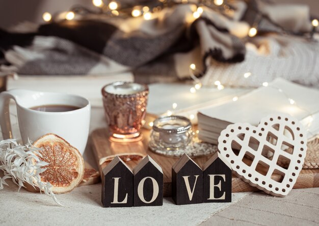 Still life with the wooden word love, a cup of drink and cozy decor details with lights.