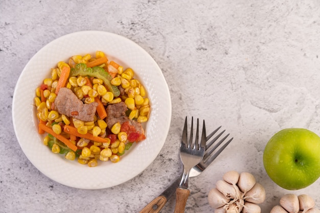 Free photo stir the corn and carrots, put the pork on the plate on the wooden plate.