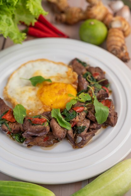 Stir fried basil liver with fried egg in a white plate.