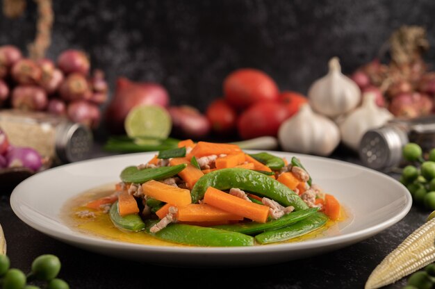 Stir fried green peas and minced pork carrots on a white plate.