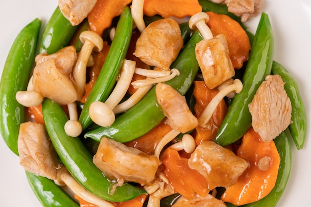 Stir-fried green peas with pork mushrooms and carrots are on a white plate