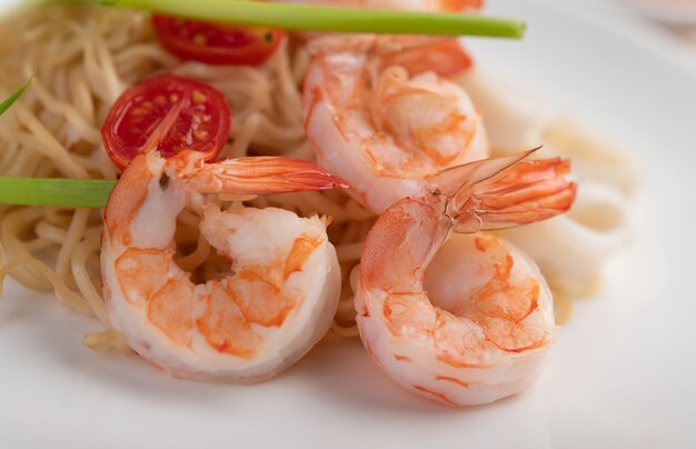 Stir-fried instant noodle with prawn and crab stick along  in a white dish.