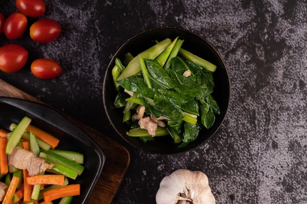 Stir-fried kale and pork belly in a plate placed on a wooden plate.