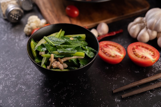 Stir-fried kale and pork belly in a plate placed on a wooden plate.