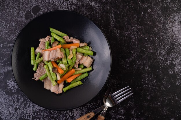 Stir-fried long beans and carrots, add pork belly, put on a black plate.